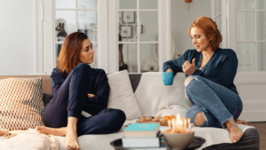 Two individuals sitting on a couch talking to each other.