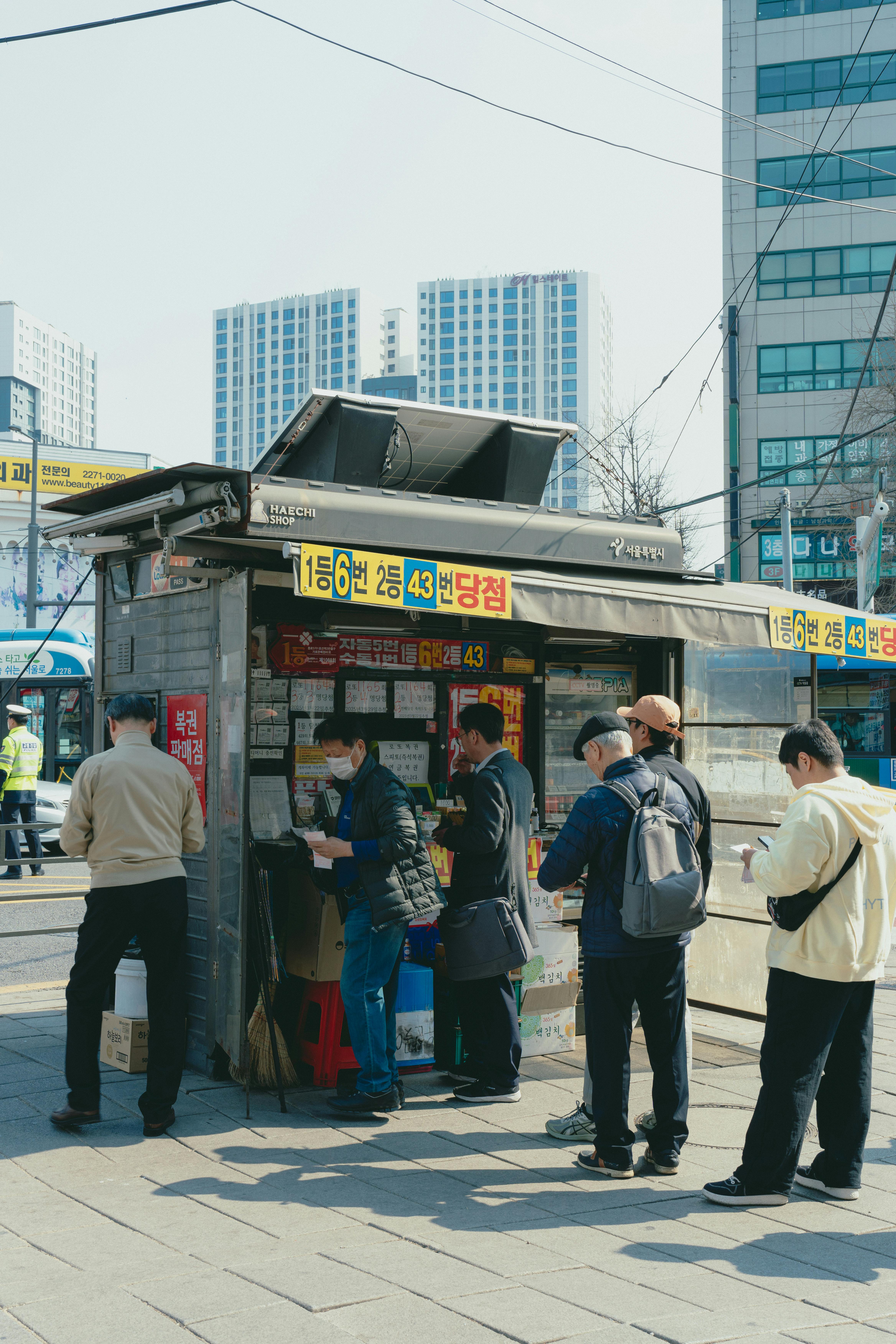 People gather at a lottery kiosk in Seoul, showcasing Korean urban life.