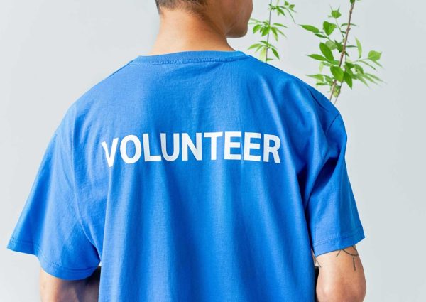 pexels-photo-8543028-8543028 A person in a blue volunteer shirt stands in front of a plant.